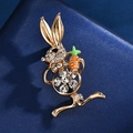 Broche lapin dorée avec cristaux étincelants tenant une carotte sur tissu bleu - Lapin avec Carotte