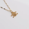 Collier en acier inoxydable doré avec pendentif tête de mort sur un fond blanc épuré - Crâne Classique à Os Croisés