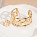 Dettaglio del set bracciale e anello a quadrifoglio dorato traforato con bordi perlati su piatto - Piccolo fiore dorato (set da due pezzi)