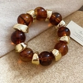 Dettaglio del bracciale con perline in resina ambra e distanziatori irregolari in metallo dorato - Caffè-Oro