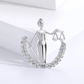 Macro shot of silver Lady Justice brooch featuring scales and sword on a white pedestal - Plain Silver