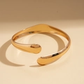 Dettaglio di un bracciale rigido dorato lucido con finitura a specchio e linee sinuose - Oro