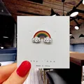 Vibrant enamel rainbow cloud brooch with cute smiley faces on a white display card - 108*Rainbow with Smiling Clouds Pin