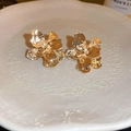 Detail view of golden metallic flower petal stud earrings on a textured ceramic plate - Gold