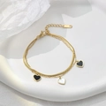 Double-layered golden bracelet with snake chain and heart-shaped pendants on white plate - Black and White Heart Bracelet / Gold