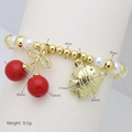 Detail eines Perlenarmbands mit rotem Kirschanhänger, goldenem Fisch und Perlen - Fisch & Kirsche Stil