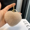 Close-up van beige hartvormige pluche sleutelhanger met gouden sluiting aan een handtas - Melkthee Kleur