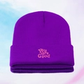 Close-up of pink You are Good embroidery on a purple knitted beanie hat texture - Purple
