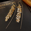 Macro shot of gold-plated leaf tassel ear threaders on a textured black display box - Leaf Tassel Ear Threader (HE11529) / Gold