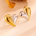 Macro view of two-tone gold and silver heart earrings on a beige textured background - Two-tone Heart Stud Earrings (H204)