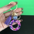 Detail of purple resin ring keychain with shell flakes, golden hardware, and matching tassel - Letter O