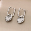 Close-up of silver heart earrings with white enamel inlay and textured rectangular hoops - Steel