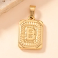 Macro shot of gold square pendant with letter B and radial texture on stone surface - Letter B