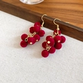 Dettaglio di orecchini a grappolo in velluto rosso con ganci dorati su supporto in legno - Stile a Grappolo d'Uva / Orecchini a Gancio Rossi