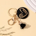 Detalle de llavero mama de madera con borla negra y anillo dorado sobre fondo minimalista - Negro