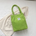 Light green corduroy bucket bag with graphic leaf label on a beige blazer background - Kiwi Green