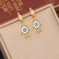 Goldene Hamsa-Ohrringe mit bösem Blick und Zirkonia auf beige Displaybox - Hamsa Hand Böser Blick Ohrringe