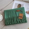 Deep green cashmere-like scarf with fringe and leather brand label on a gray sofa - Dark Green
