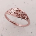 Primer plano detallado de un anillo de sello de oro rosa con grabado floral superior - US 5 / Rosa oro