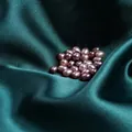 Perles d'eau douce ovales lavande polies sur un tissu de soie vert foncé luxueux - Violet