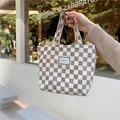 Detail der Cord-Schachbrett-Lunchtasche mit Pleasant Time-Etikett in einem Café-Ambiente - Hellbraunes Schachbrett