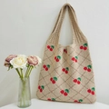 Knitted beige tote bag with red cherry pattern hanging on a minimalist white wall - Khaki