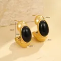 Detalle de pendientes de aro dorados con gran piedra negra ovalada sobre fondo de piedra - Oro de 18K / Negro