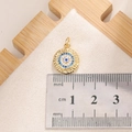 Macro detail of 10mm gold Evil Eye pendant with blue zircon stones on a white surface - E009G