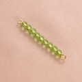 Macro shot of green faceted crystal beads with golden metal connectors on pink fabric - Light Green