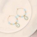 Primer plano de aros dorados con cuentas azules y dijes de ojo turco sobre cerámica blanca - Estilo de Ojo de Gato (3#眼睛)