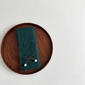 Close-up of dark green ribbed knit scarf with brown bow and white faux fur pom-poms - Dark Green