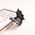 Detailed close-up of a black bat-shaped hair claw clip on a stylish book edge - Black