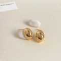 Primer plano de pendientes ovalados bañados en oro de 18K sobre un fondo crema suave - Gota de Agua Curva Dorada Bañada en Oro de 18K