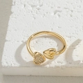 Minimalistischer goldener Herzring mit Kristallbesatz auf steinernem Untergrund - Doppelherz-Ring