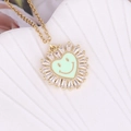 Macro detail of gold heart necklace with zircon border and green enamel smiley face pendant - Green