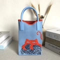 Bolso de mano de punto azul claro con gato naranja en un entorno acogedor y cálido - Azul y Naranja