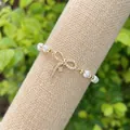 Macro detail of 18K gold bow charm with pavé crystals on a white pearl bracelet - Style 2(2)