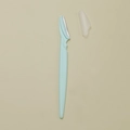 Light green eyebrow razor with safety guard and translucent cap on beige background - Blue