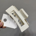 Close-up of a cream-colored hollow square hair claw clip held against a grey wall - Beige