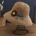 Detail of woven straw hat with crochet flowers and green leaves on a display stand - Khaki