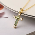 Macro shot of 18K gold cross necklace with green zircon and heart-shaped gems on soft cloth - Green