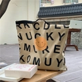 Khaki canvas shopper met smiley en zwarte letters op een houten terras buitenkant - Khaki