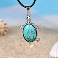 Turtle pendant necklace featuring green turquoise stone and black cord on beach sand - Turquoise