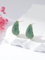 Close-up of gold teardrop earrings with pavé green gemstones on stone stand - Green