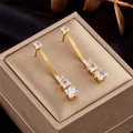 Golden snake chain earrings with square green crystals displayed on a luxury jewelry box - Clear