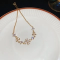 Detalle de pulsera dorada ajustable con dijes de circonita en forma de copo y flor de lis - Estilo Flor de Lis Cruz Dorada / Dorado