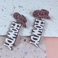 Detailed shot of glittery brown cowboy hat earrings with white HOWDY lettering charms - Multicolor/Brown Glitter