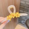 Milchteefarbene Blumen-Haarklammer aus Acryl mit gelben Akzenten in der Hand gehalten - Gelb