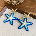 Detailweergave van handgemaakte raffia zeester oorbellen met gouden metalen sterren. - 36# Wit-Blauw (Overlappende Zeester)