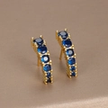 Orecchini curvi dorati con gemme blu rotonde su sfondo marrone strutturato - Strass Blu Dorato (E1134)